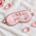 Pink satin sleep mask on white linen with rose petals